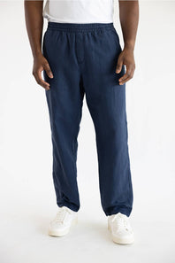 A person wearing loose navy blue drawstring pants with white sneakers, shown from the waist down against a plain white studio background.