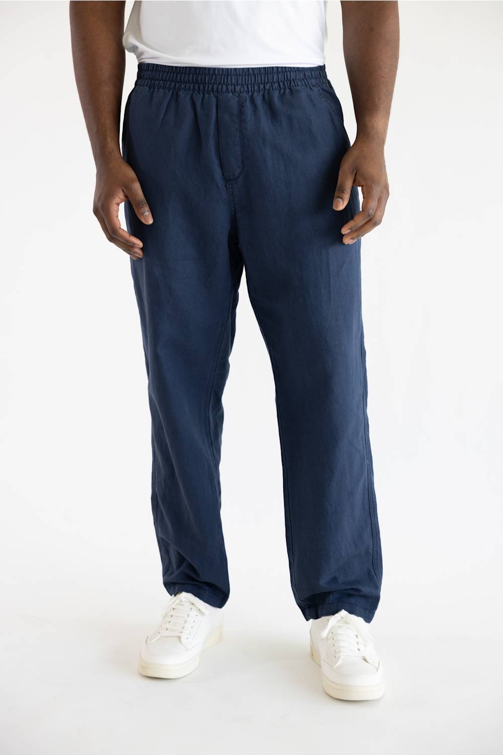 A person wearing loose navy blue drawstring pants with white sneakers, shown from the waist down against a plain white studio background.
