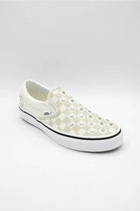 A white slip-on platform sneaker featuring a checkerboard pattern on the side and rows of silver metal studs across the toe box, shown against a light gray studio background.