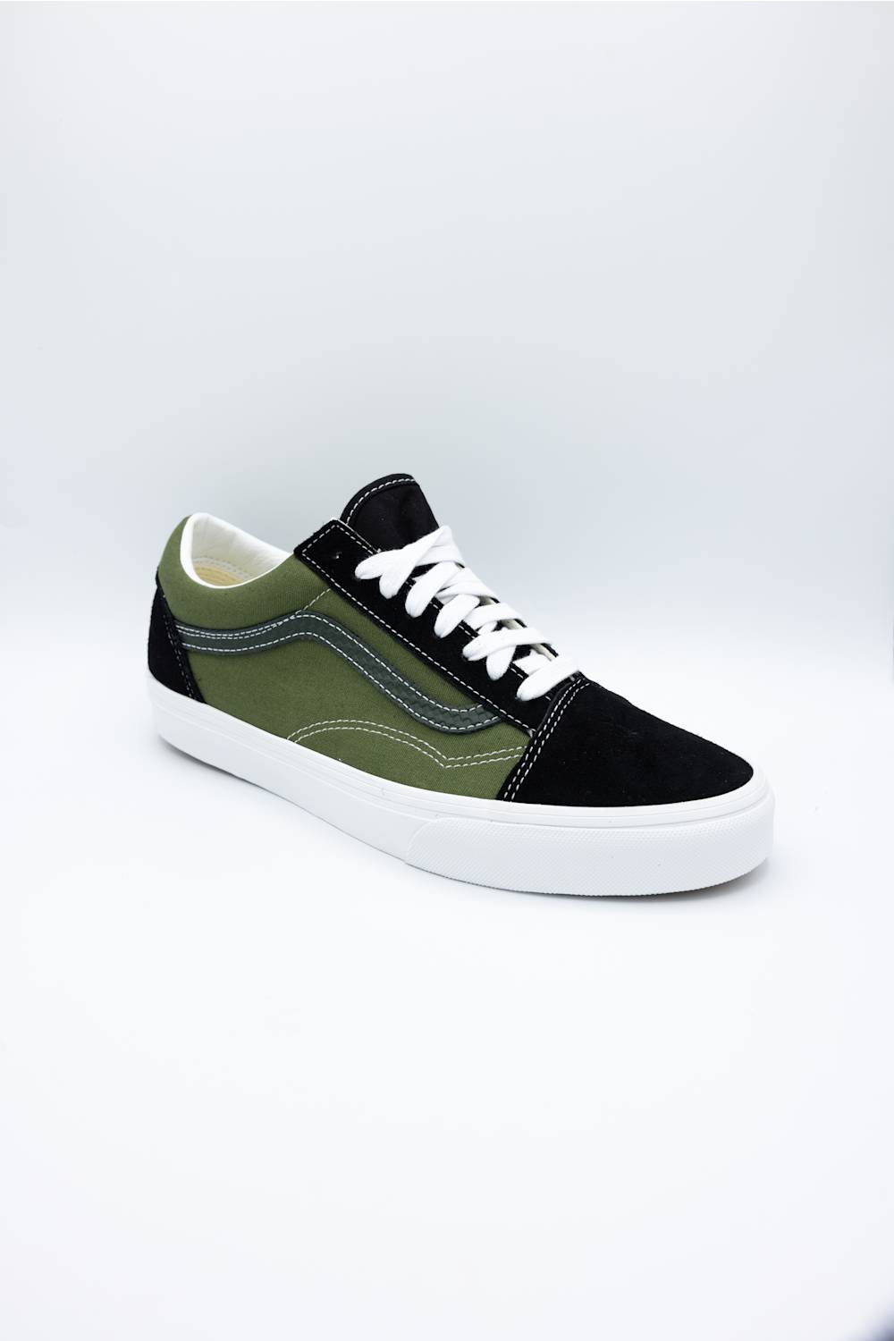 A low-top platform sneaker with an olive green and black suede upper, white laces, and a thick white platform sole, photographed on a light gray studio background.