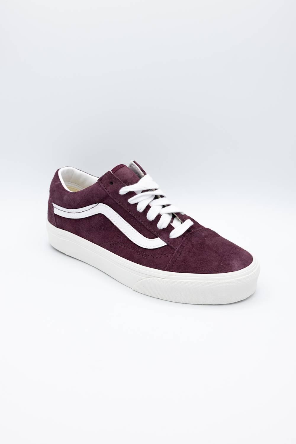 A single Vans low-top sneaker in dark burgundy suede with white laces and a white rubber side stripe and sole, shown on a light gray studio background.