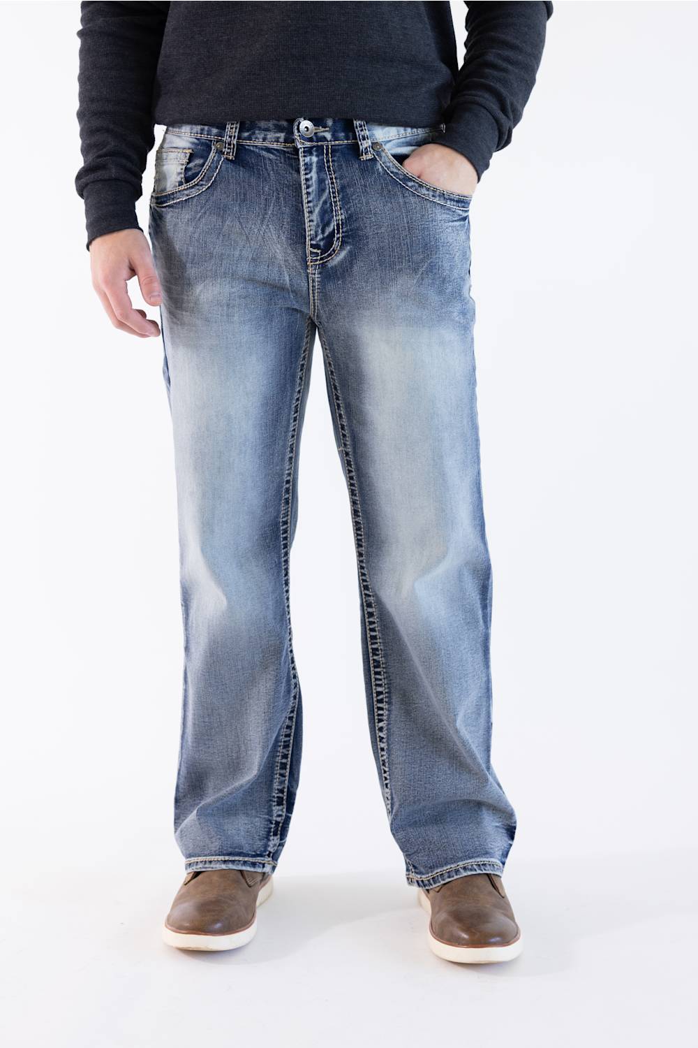 A three-quarter view from the waist down of a man wearing a pair of "Weller Loose Straight" fit True Luck jeans. The denim is a distressed medium-light blue wash with heavy whiskering on the thighs and fading on the knees. He is also wearing a dark grey, long-sleeved shirt and brown shoes. The background is a solid, light grey.