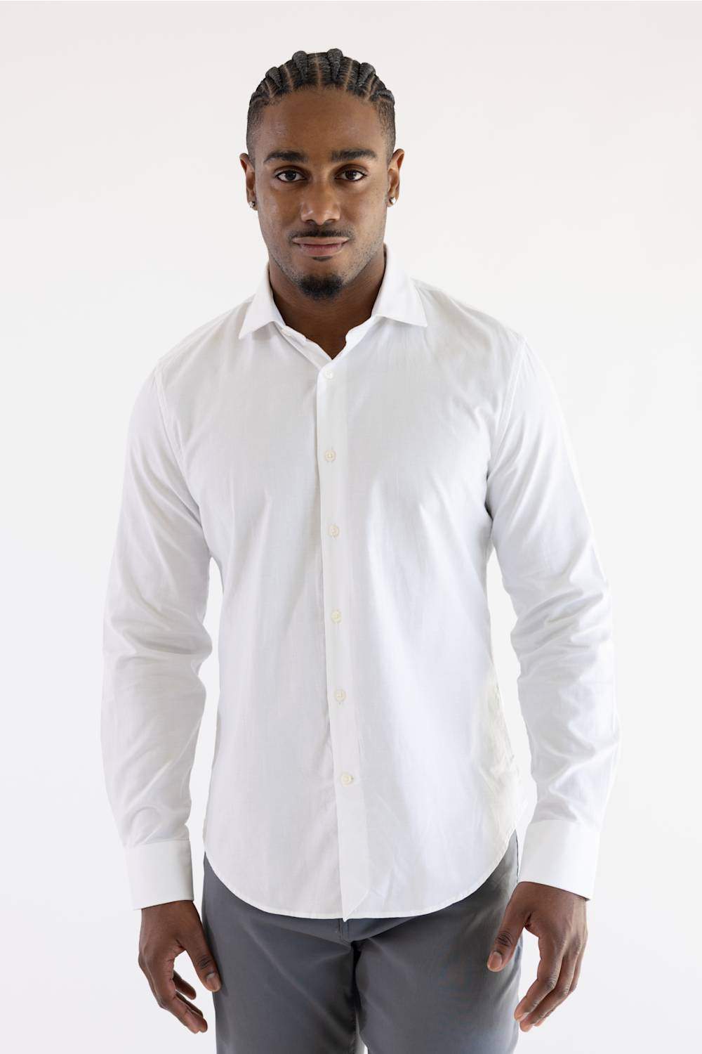 A man wearing a white long-sleeve button-down dress shirt and gray trousers, standing against a plain white studio background.