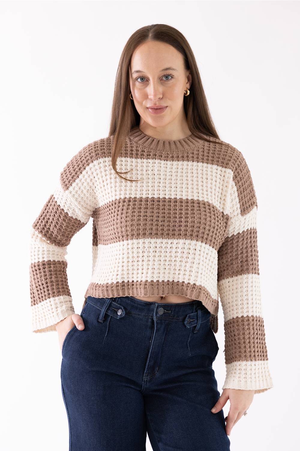 Woman wearing a Pink Rose wide tan-and-white-striped crewneck sweater with long sleeves, facing forward with her hand in her dark blue jeans pocket.