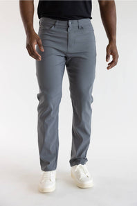 A person wearing slim-fit gray trousers, paired with a black top and white sneakers, standing against a plain light gray studio background.