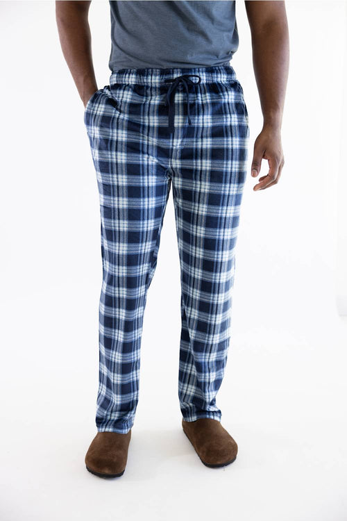 A person wearing blue and white plaid pajama pants with a drawstring waist, paired with a gray t-shirt and brown slippers, shown from the waist down on a white studio background.