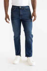 A person wearing dark blue slim-fit jeans with a white t-shirt and white sneakers, shown from the waist down against a plain white studio background.