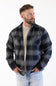 A man modeling the Weatherproof Vintage Lumberjack Plaid Shirt Jacket in "Phantom Night" (charcoal and dark navy plaid) worn open over a beige crewneck sweater and light-wash jeans with his hands in his pockets against a white studio background.