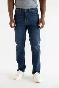 A person wearing dark blue slim-fit jeans with a gray t-shirt and white sneakers, shown from the waist down against a plain white studio background.