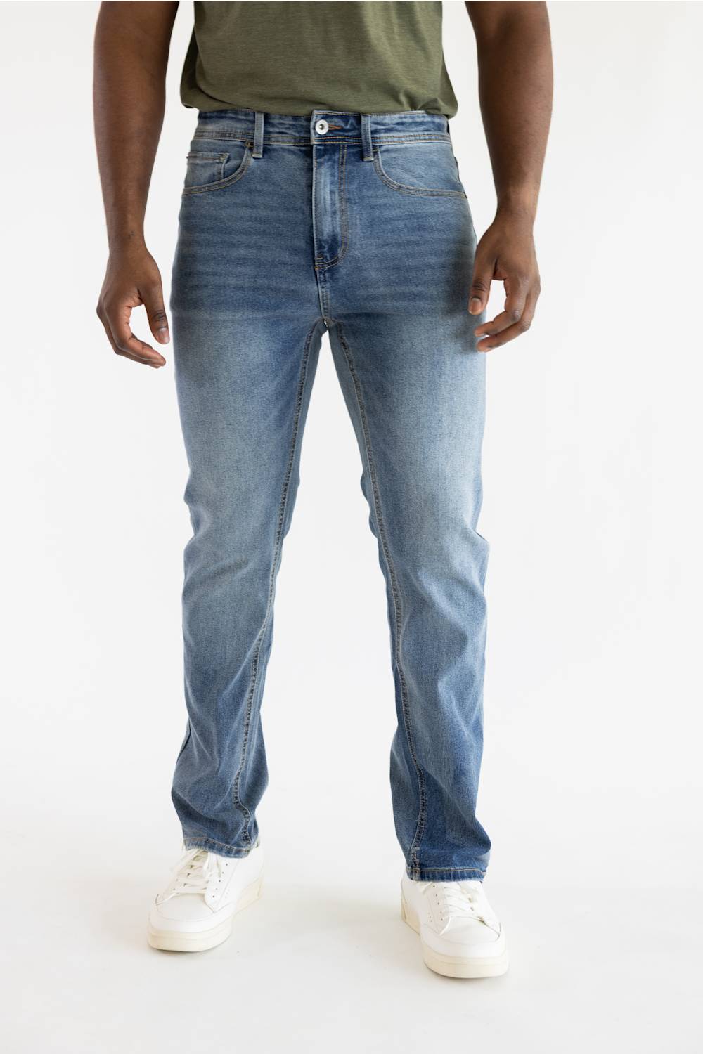 A person wearing light blue slim-fit jeans with a faded wash, paired with an olive green t-shirt and white sneakers, shown from the waist down against a plain white studio background.
