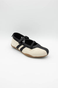 A single Mary Jane style shoe with a cream colored upper, black leather trim and strap, and a brown gum sole, shown against a plain light gray background.