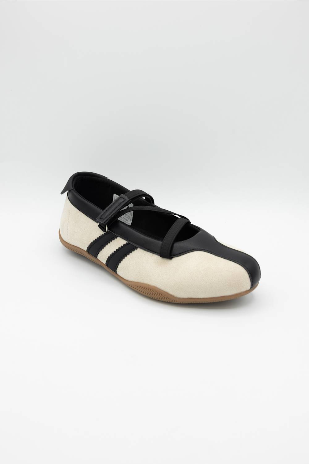 A single Mary Jane style shoe with a cream colored upper, black leather trim and strap, and a brown gum sole, shown against a plain light gray background.
