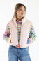 A woman wearing a pale pink puffer vest over a colorful striped knit sweater and blue jeans, photographed against a plain white studio background.
