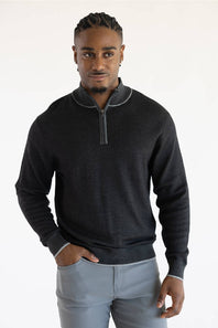 A man wearing a dark charcoal gray quarter-zip sweater with light gray piping details on the collar and cuffs, paired with light gray trousers, against a plain white studio background.