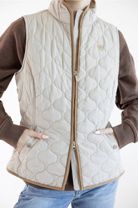 A quilted beige puffer vest with a brown zipper and trim, worn over a brown long-sleeve shirt and blue jeans.