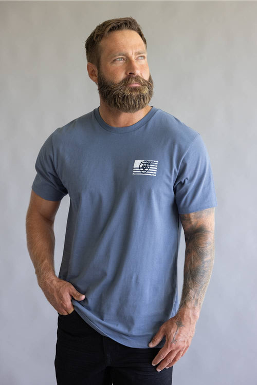 Front view of a bearded man wearing a slate blue Ariat t-shirt with a chest graphic.