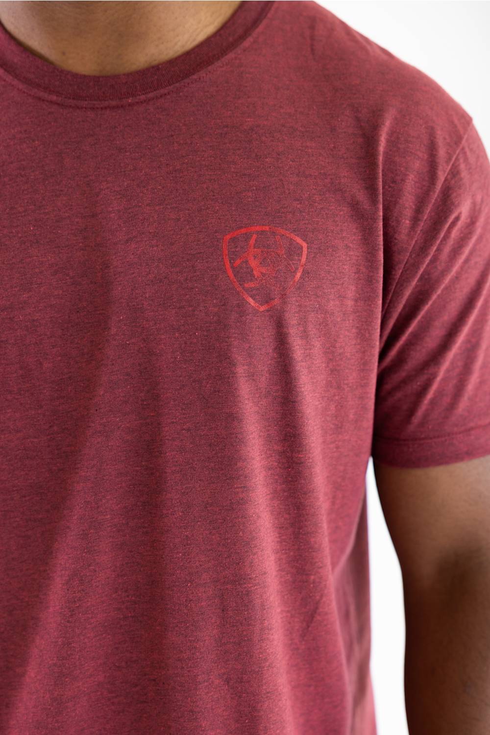 A close-up of a person wearing a heathered red crew-neck t-shirt with a subtle tonal Ferrari shield logo on the left chest.