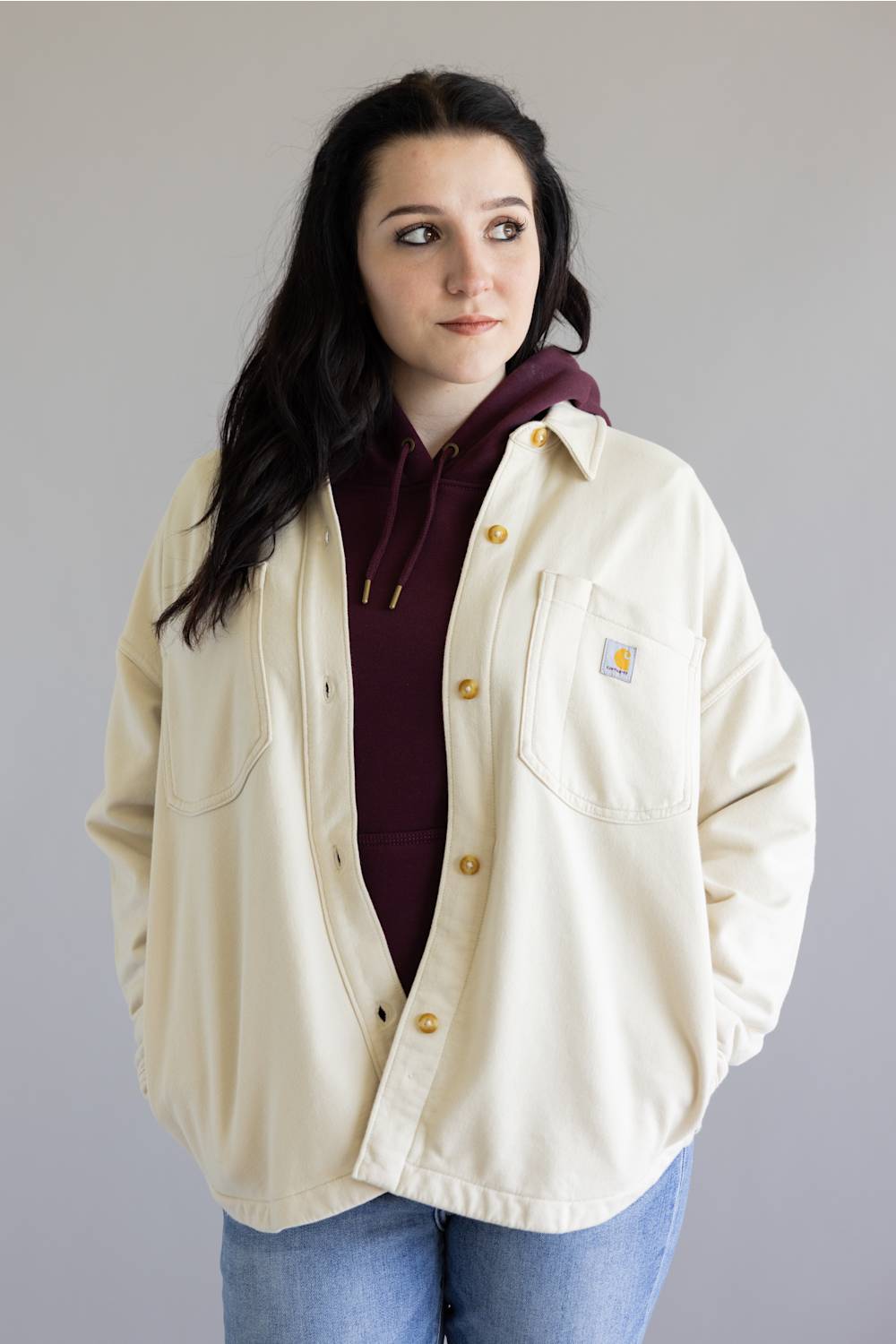 Person wearing a beige Carhartt jacket over a maroon hoodie on a plain background
