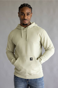 A man wearing a light cream-colored Carhartt hoodie with blue jeans, standing against a neutral gray studio background.