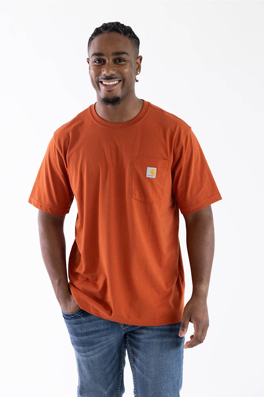 A man wearing a bright orange short-sleeve pocket t-shirt with a small Carhartt logo on the chest pocket, paired with blue jeans, against a plain white background.