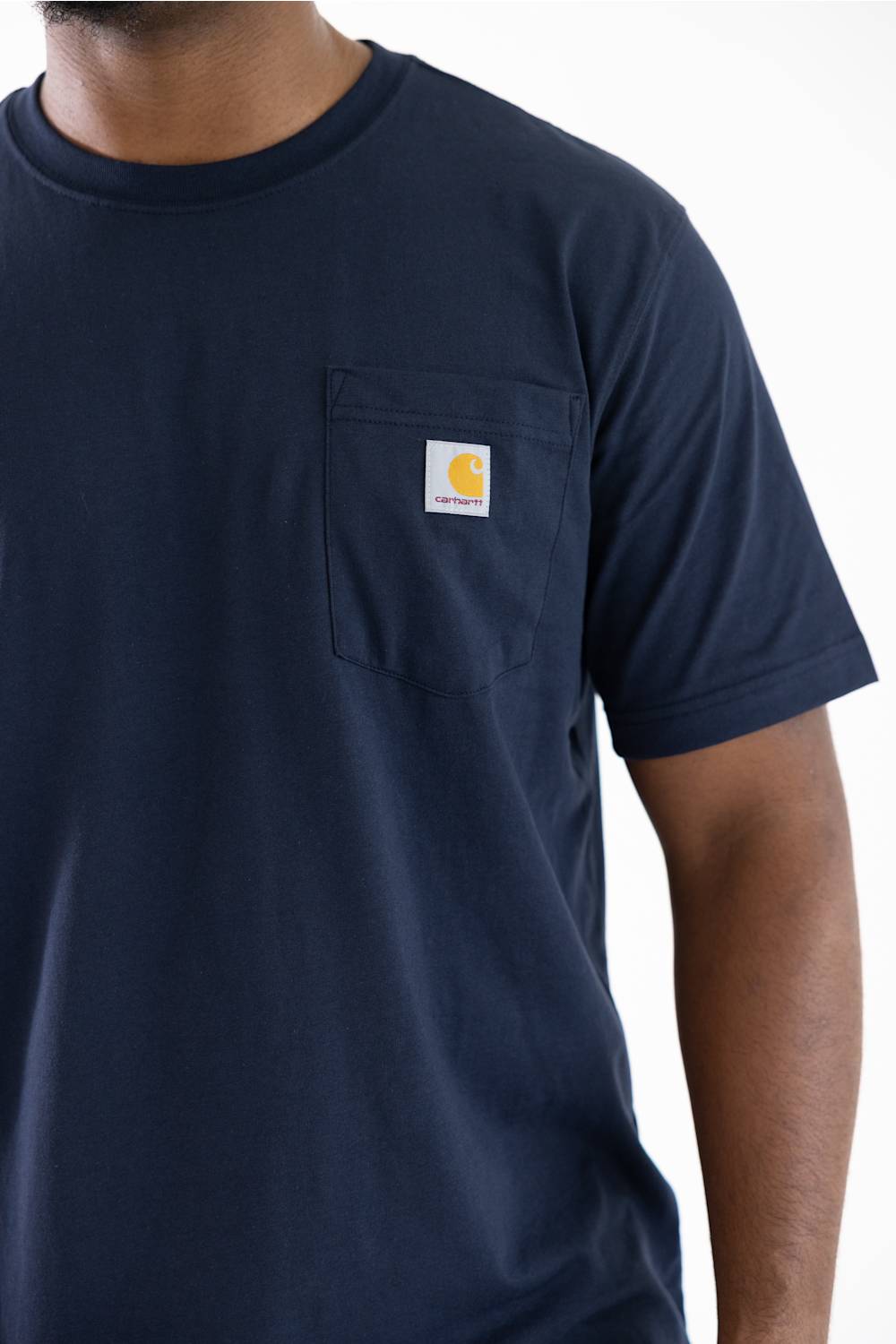 Close up view of a man wearing a navy blue short-sleeve pocket t-shirt with a small Carhartt logo on the chest pocket