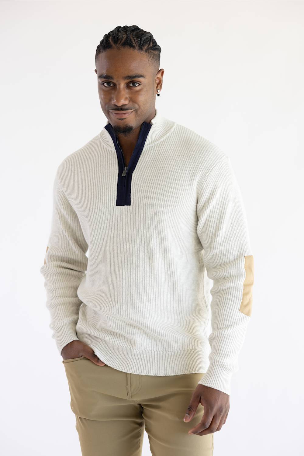 A man wearing a cream ribbed knit quarter-zip sweater with navy and tan patchwork details on the shoulders and sleeves, paired with khaki pants, against a plain white studio background.