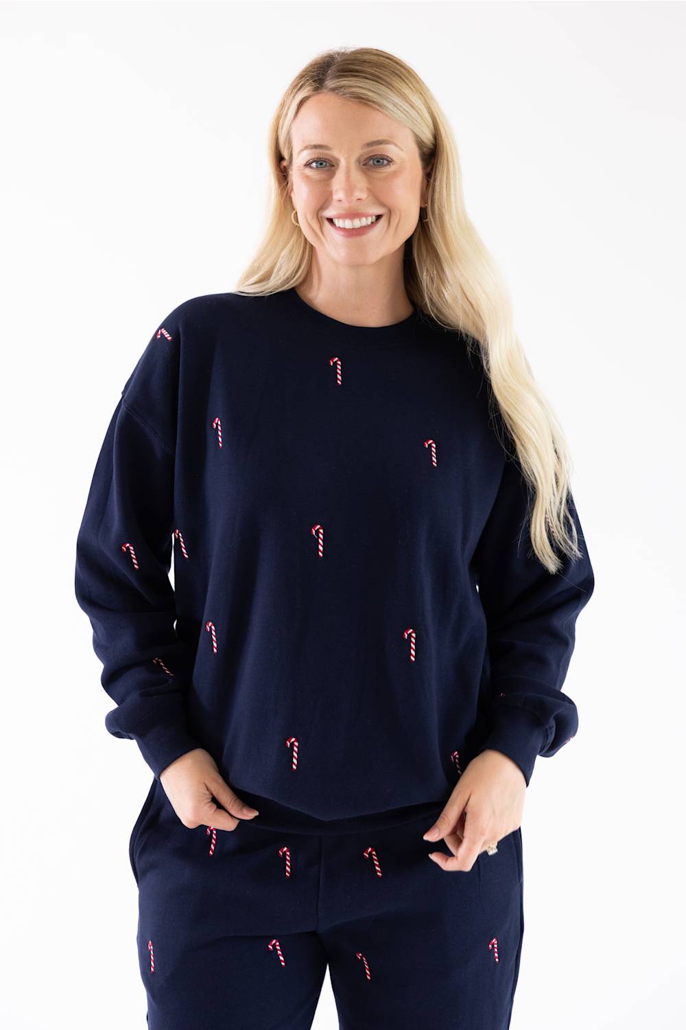 Front view of a woman wearing a navy blue crewneck sweatshirt with small red and white candy cane embroidery scattered across the front, with matching sweatpants.