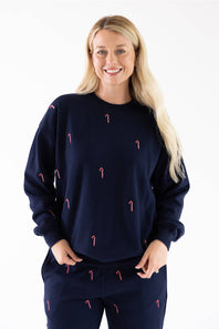 Front view of a woman wearing a navy blue crewneck sweatshirt with small red and white candy cane embroidery scattered across the front, with matching sweatpants.