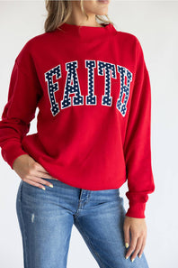Close-up view of a woman wearing the red 1897 Active Faith mock neck sweatshirt, highlighting the navy blue "FAITH" applique lettering with white polka dots across the chest.