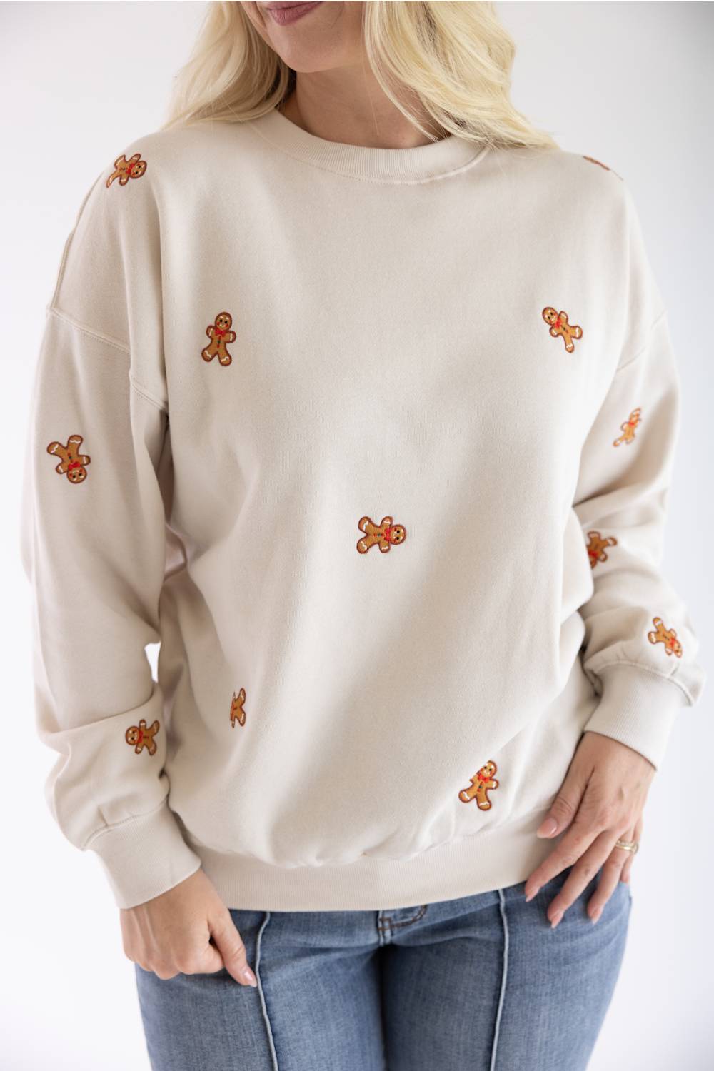 Detail shot of a woman in a beige fleece sweatshirt with embroidered gingerbread men.
