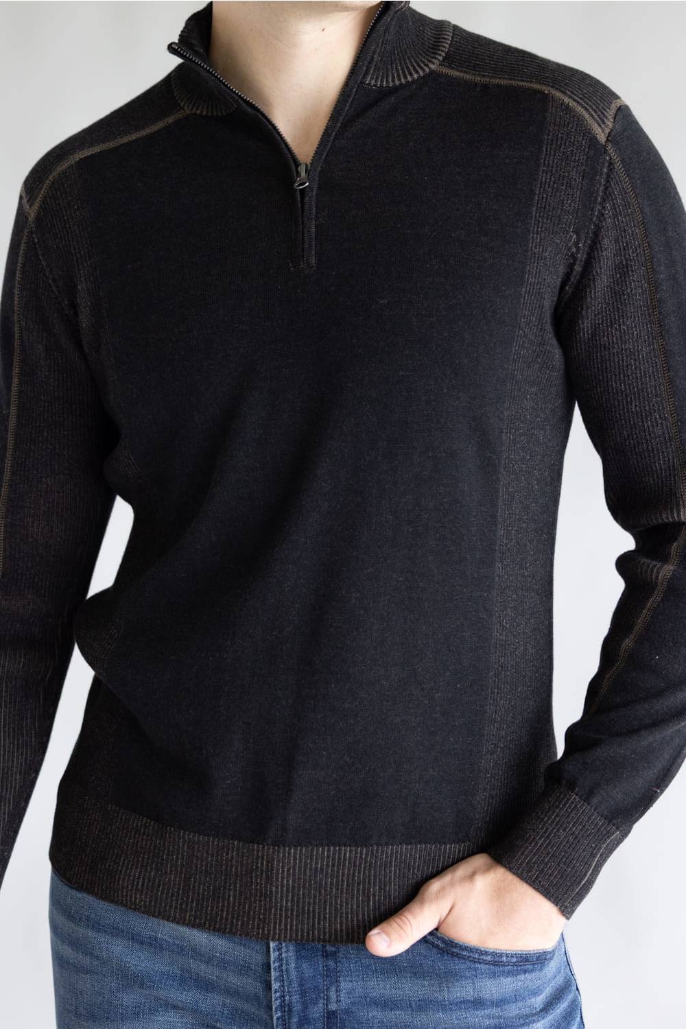 A man wearing a dark charcoal gray quarter-zip knit sweater with ribbed trim, paired with blue jeans, shown from the neck down against a light gray background.