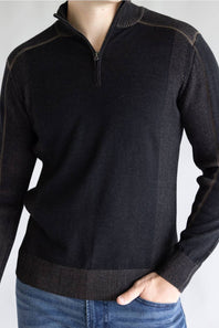A man wearing a dark charcoal gray quarter-zip knit sweater with ribbed trim, paired with blue jeans, shown from the neck down against a light gray background.