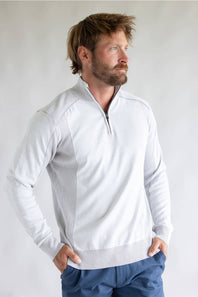 A man wearing a white quarter-zip pullover sweater with textured knit side panels and ribbed trim, paired with blue pants, photographed against a light gray studio background.