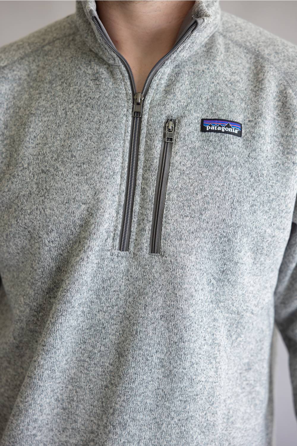 Close-up of a person wearing a heather gray quarter-zip fleece pullover with a visible Patagonia logo patch on the chest.