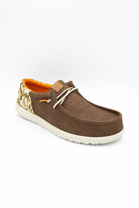 A brown suede slip-on shoe with a patterned heel, white laces, and a white textured sole, shown on a white background.