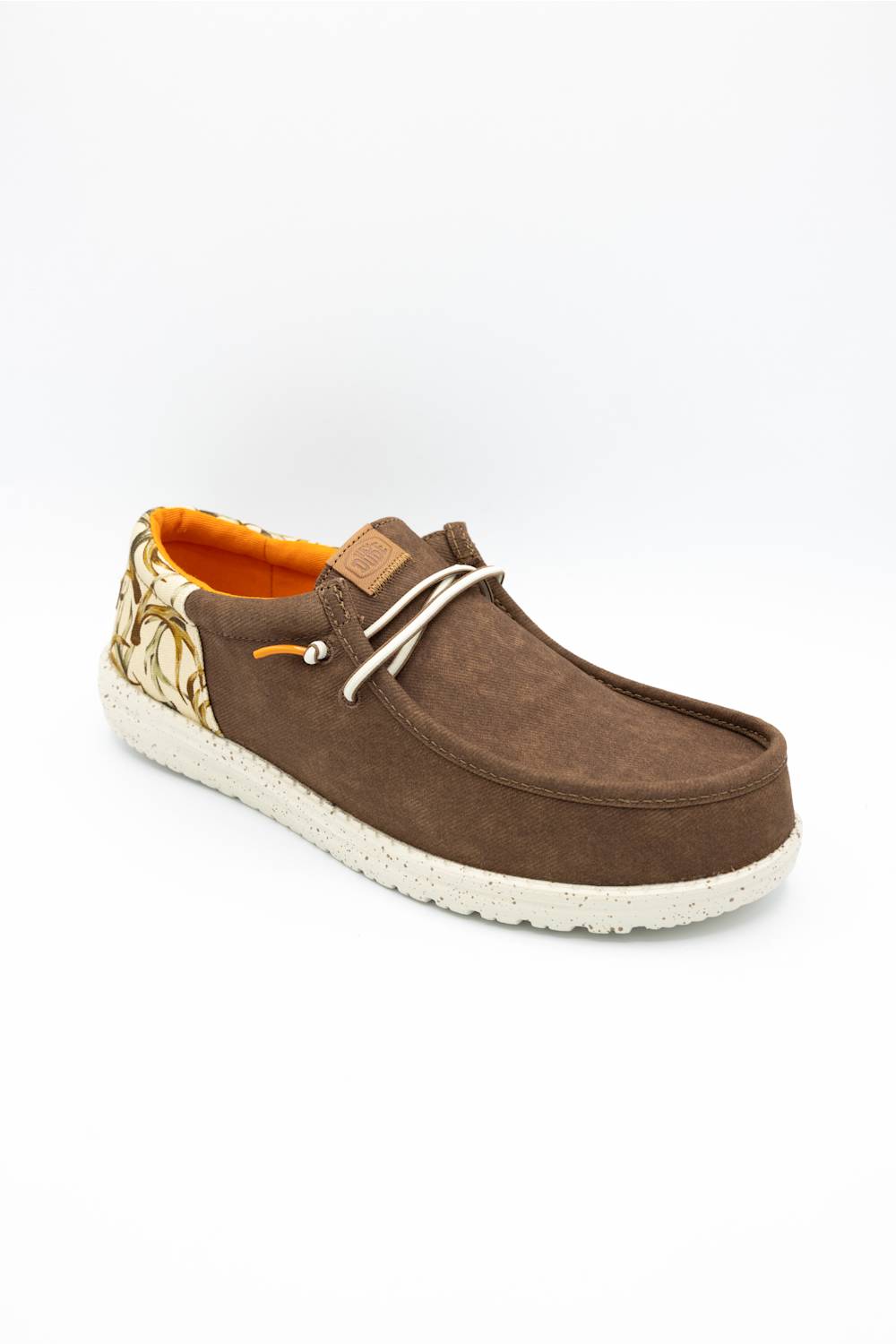 A brown suede slip-on shoe with a patterned heel, white laces, and a white textured sole, shown on a white background.