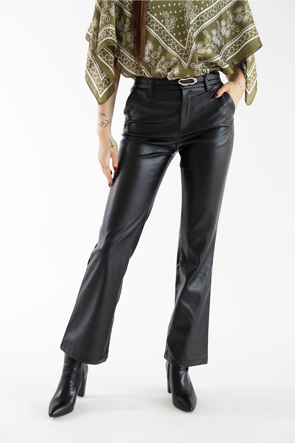 A model wearing black faux-leather flare pants with a matching black belt, paired with a green patterned top and black ankle boots, against a plain white studio background.