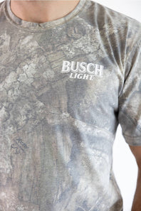 Close-up front view of a man wearing a camo JEDCo t-shirt featuring a white Busch Light logo printed on the left chest.