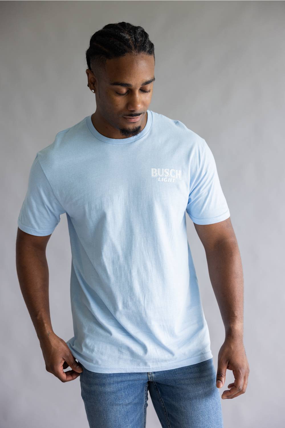 A man wearing a light blue crewneck t-shirt with a large graphic on the back. The graphic features the words 'BUSCH LIGHT' in blue, a white goose with yellow wings, and a yellow sun over blue waves.