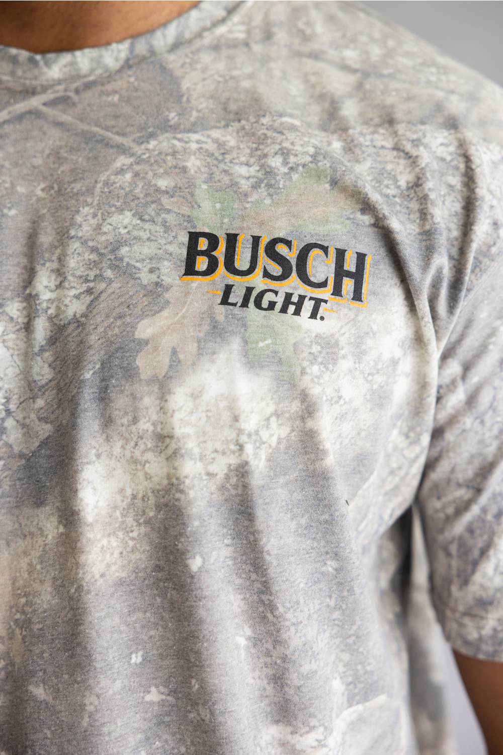 Close-up of a person wearing a Busch Light t-shirt with a gray and white tie-dye camouflage pattern and a black and gold logo on the chest.