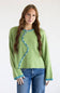 A woman modeling a light green knit sweater with a distinctive wavy teal trim and white bead details down the front, paired with blue jeans against a plain white background.