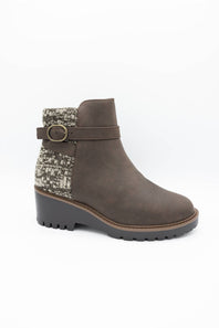 A brown suede ankle boot with a textured gray and white knit pattern panel on the side, a matching brown strap with a gold-tone buckle, and a chunky dark gray lug sole.
