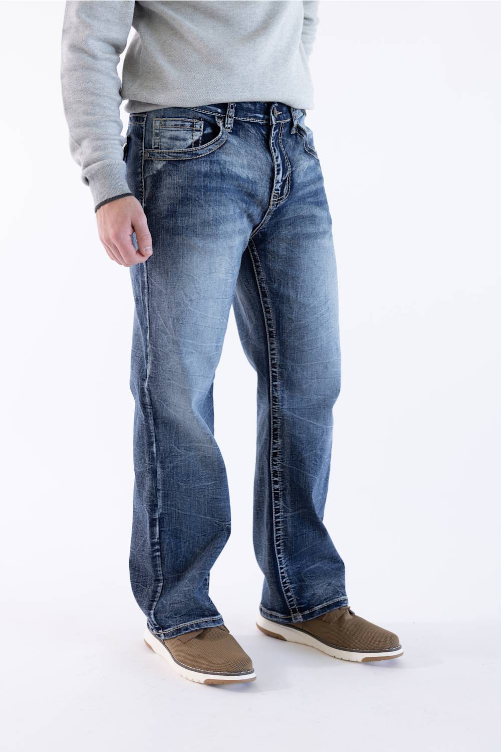 Men's medium wash straight-leg jeans featuring a side-profile view, subtle whiskering, and pairing with a grey crewneck sweater and brown casual shoes.