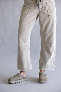 A person wearing light beige corduroy cropped pants with a drawstring waist and side pockets, paired with taupe slip-on shoes, photographed against a plain light gray studio background.