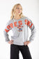 A blonde woman wearing a light gray crewneck sweatshirt with 'APRES SKI' in orange text and a cartoon bear skier graphic, paired with black jeans, against a plain white background.
