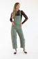 Front view of model wearing Aaron & Amber Slouchy Denim Overalls for Women in Olive featuring a relaxed barrel leg fit, classic chest bib pocket, and adjustable straps over a black patterned long-sleeve top paired with burgundy sneakers.