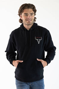 A man wearing a black pullover hoodie with a small bull skull logo on the left chest, paired with blue jeans, against a plain white background.