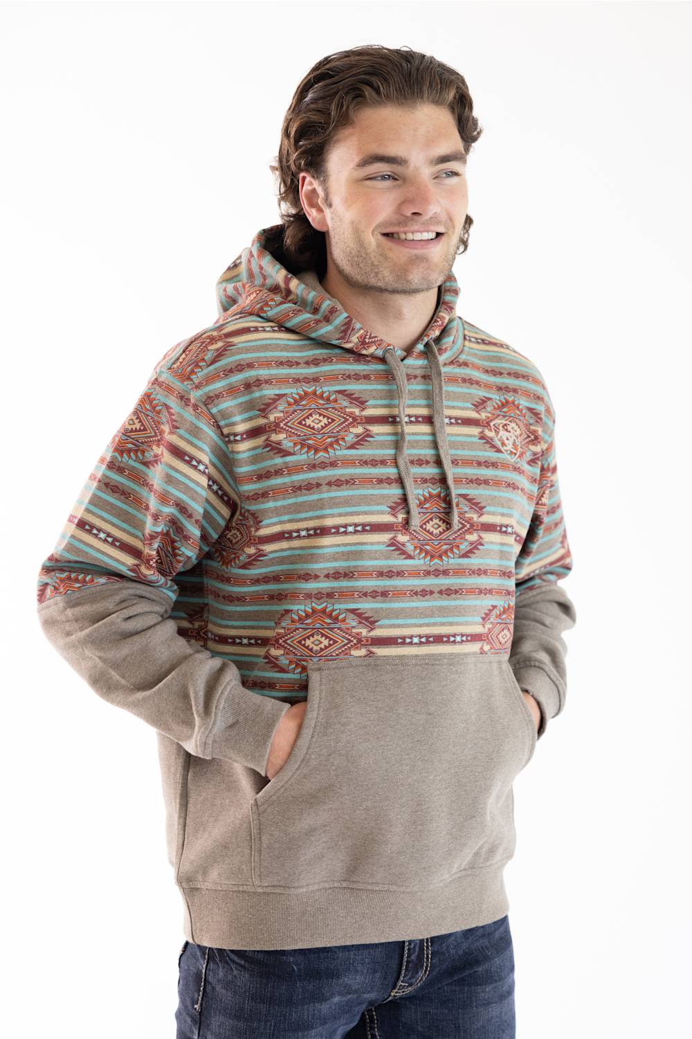 A man wearing a patterned hoodie with a beige kangaroo pocket and blue jeans, standing against a white studio background.