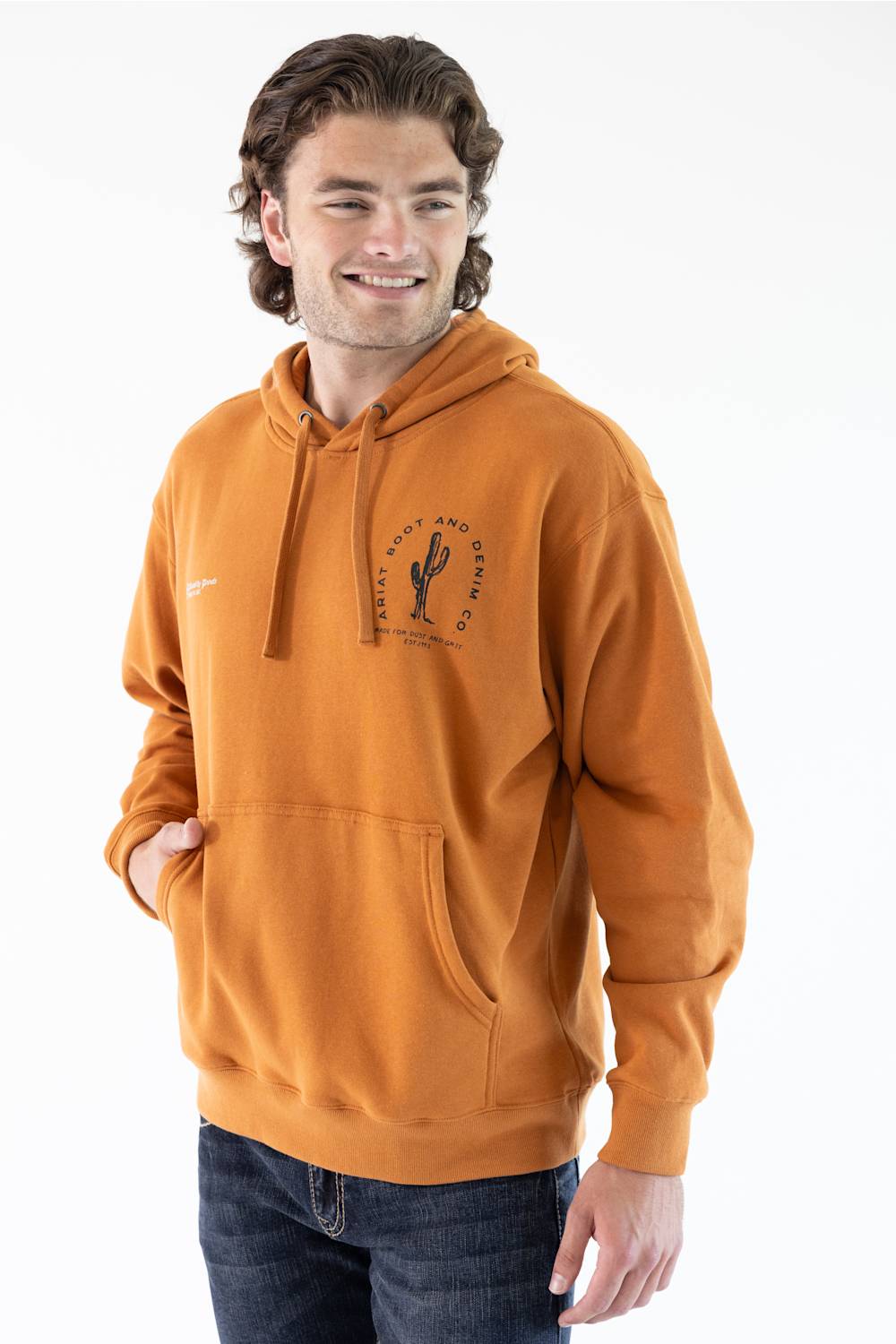 A man wearing an adobe brown hoodie with a black desert cactus graphic on the left chest, paired with dark blue jeans, photographed against a solid white background.