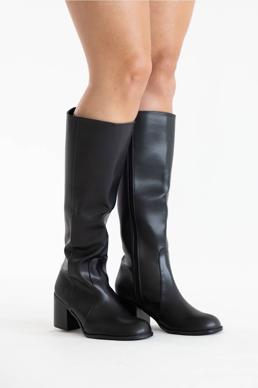 A pair of black leather knee-high boots with block heels, shown on a model's feet against a plain white studio background.